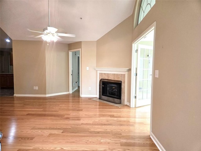 unfurnished living room with light wood-style floors, a tile fireplace, baseboards, and ceiling fan