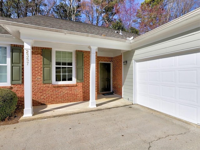 property entrance with driveway, roof with shingles, an attached garage, a porch, and brick siding