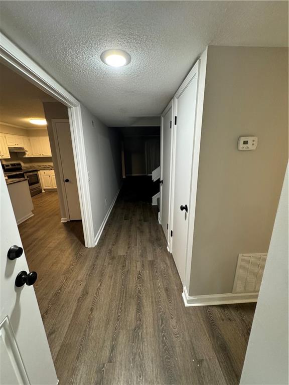 corridor with a textured ceiling and dark wood-type flooring