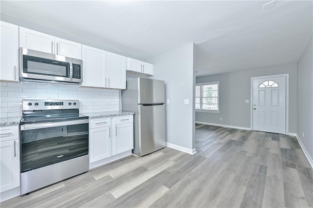 kitchen with backsplash, appliances with stainless steel finishes, white cabinetry, and light wood-type flooring