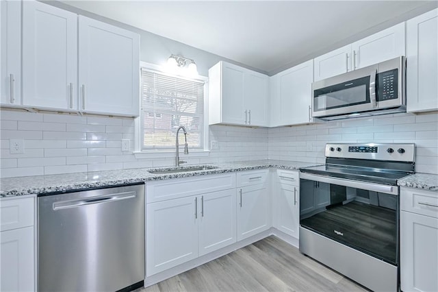 kitchen with tasteful backsplash, white cabinets, appliances with stainless steel finishes, and a sink