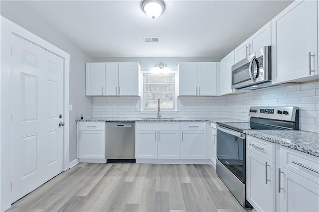 kitchen with a sink, light stone countertops, white cabinetry, and stainless steel appliances