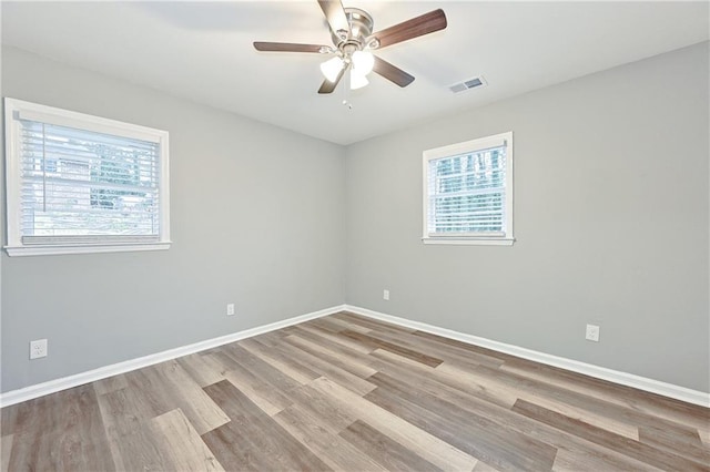 empty room with visible vents, wood finished floors, baseboards, and ceiling fan