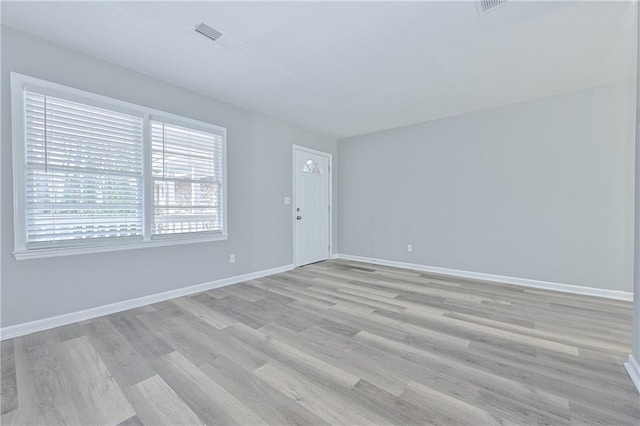 empty room featuring light wood-style floors, baseboards, and visible vents