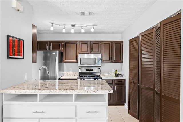 kitchen with dark brown cabinetry, light tile patterned floors, appliances with stainless steel finishes, and a textured ceiling