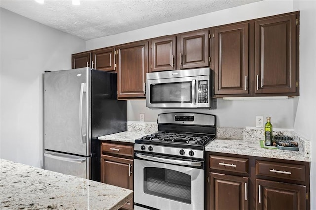 kitchen with a textured ceiling, light stone counters, dark brown cabinets, and stainless steel appliances