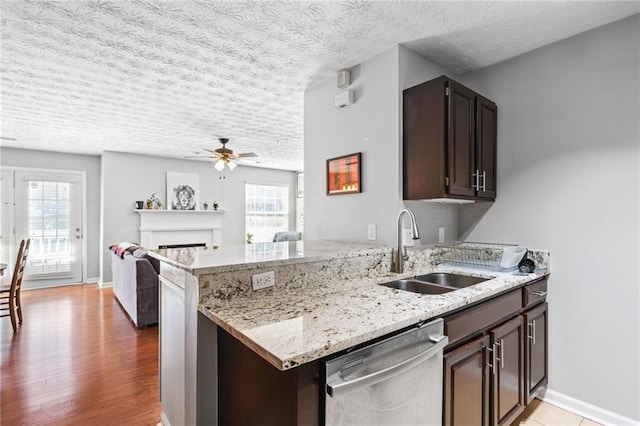 kitchen featuring a ceiling fan, light stone countertops, a sink, dark brown cabinetry, and stainless steel dishwasher