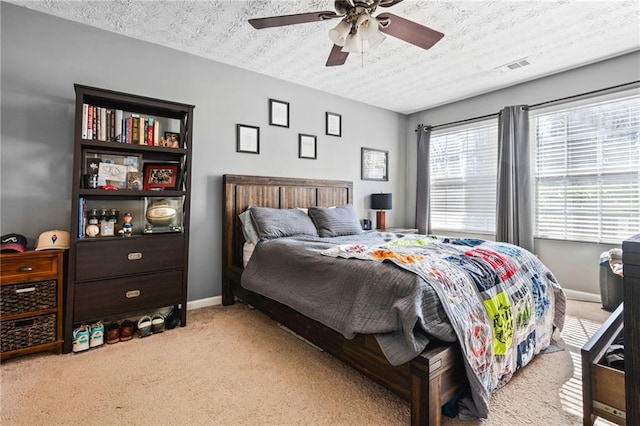 bedroom featuring a ceiling fan, baseboards, carpet, visible vents, and a textured ceiling