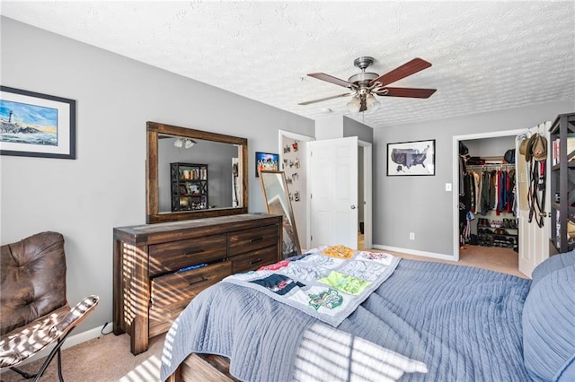 bedroom with carpet, baseboards, ceiling fan, a textured ceiling, and a walk in closet