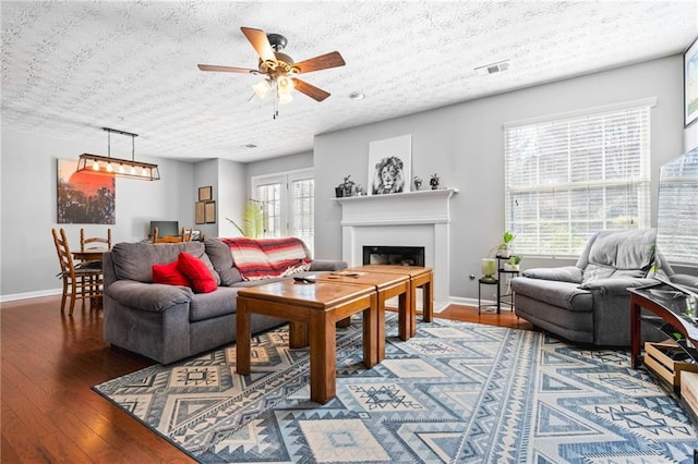 living area featuring visible vents, baseboards, ceiling fan, a fireplace, and wood-type flooring