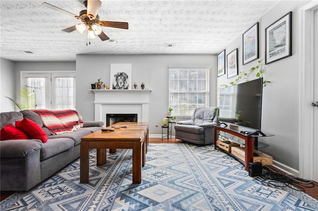 living area featuring visible vents, a fireplace, baseboards, and a ceiling fan