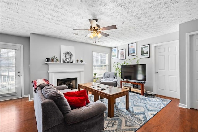 living room with a glass covered fireplace, baseboards, wood finished floors, and ceiling fan