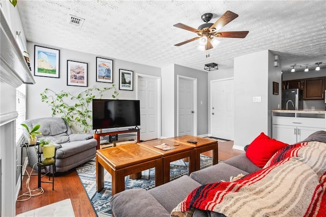 living room with wood finished floors, baseboards, visible vents, ceiling fan, and a textured ceiling