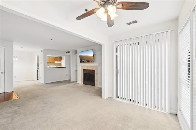 unfurnished living room featuring a tiled fireplace, light carpet, and ceiling fan