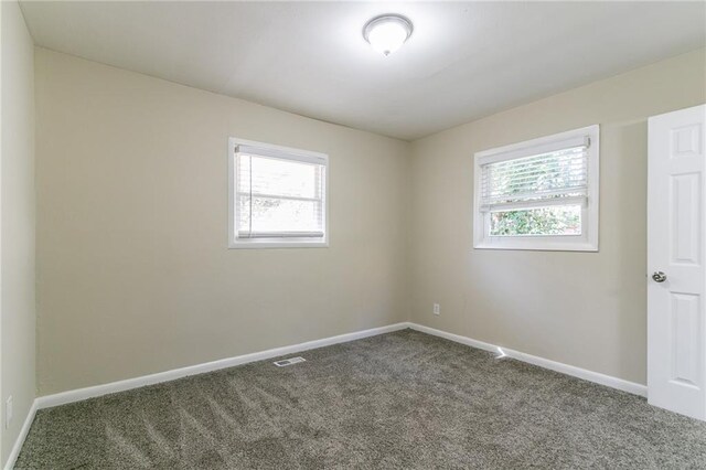 spare room with a wealth of natural light and dark colored carpet