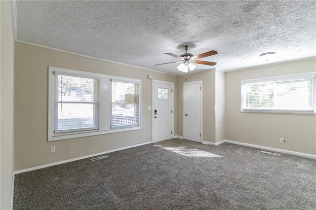 interior space featuring plenty of natural light, a textured ceiling, and dark colored carpet