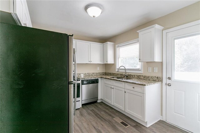 kitchen with sink, light stone counters, wood-type flooring, white cabinets, and appliances with stainless steel finishes