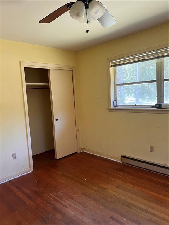 unfurnished bedroom with a baseboard radiator, dark wood-type flooring, ceiling fan, and a closet