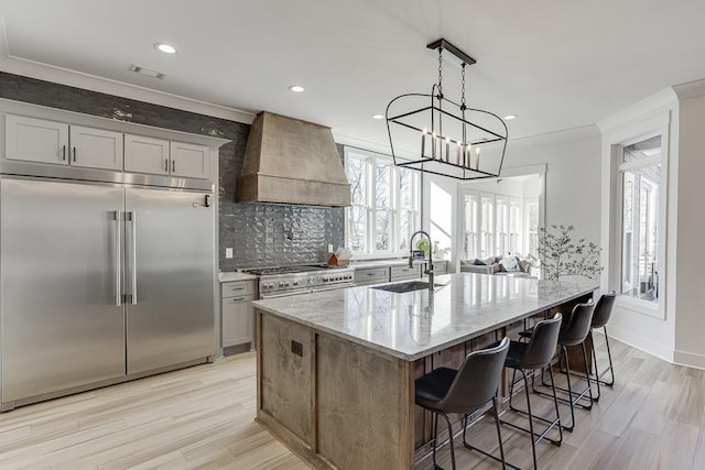 kitchen featuring a kitchen breakfast bar, custom range hood, sink, light stone countertops, and high end appliances