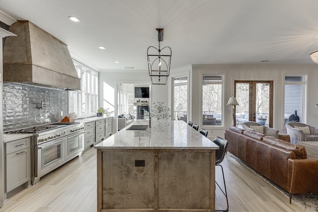 kitchen with french doors, sink, premium range hood, light stone countertops, and range with two ovens