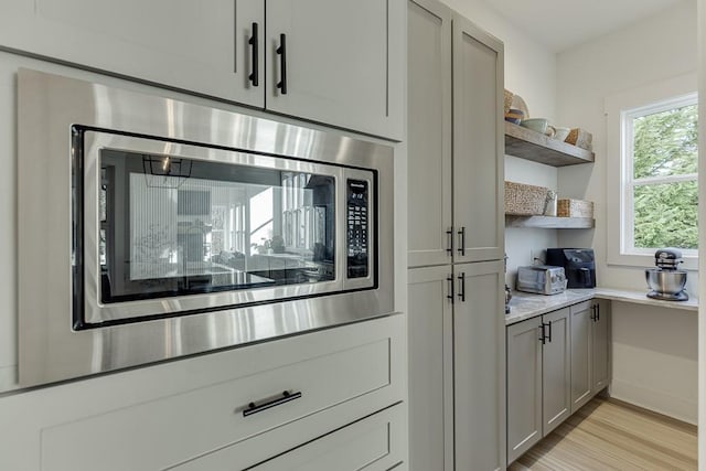 room details featuring light stone countertops, stainless steel microwave, gray cabinetry, and light wood-type flooring