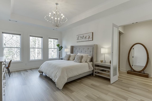 bedroom with light wood-type flooring, a chandelier, and a raised ceiling