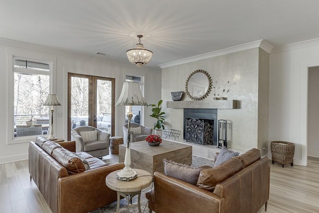 living room featuring light hardwood / wood-style floors, french doors, ornamental molding, and a chandelier