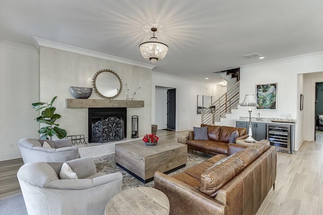 living room with beverage cooler, ornamental molding, a chandelier, and light wood-type flooring