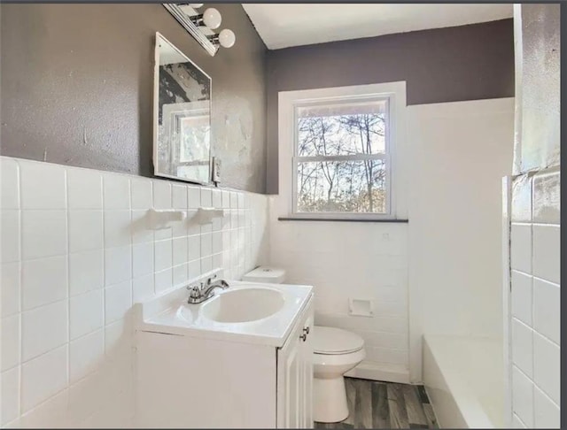 full bath with a washtub, toilet, vanity, wood finished floors, and tile walls