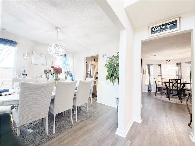 dining space with a notable chandelier, a textured ceiling, baseboards, and wood finished floors