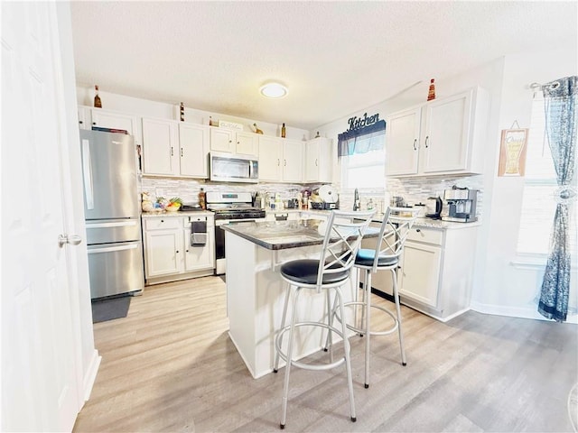 kitchen with white cabinets, a kitchen island, appliances with stainless steel finishes, a kitchen breakfast bar, and light wood-type flooring