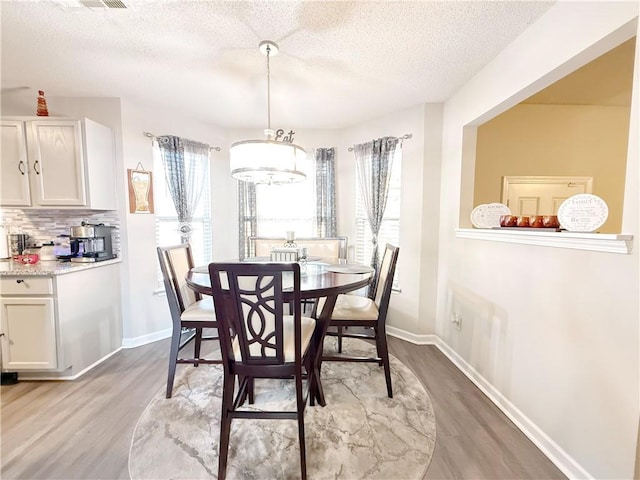 dining room featuring a textured ceiling, light wood finished floors, a wealth of natural light, and baseboards