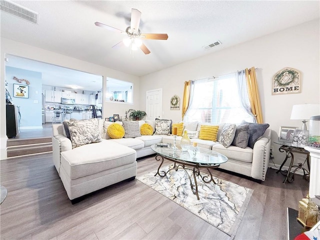 living area with a ceiling fan, baseboards, visible vents, and wood finished floors