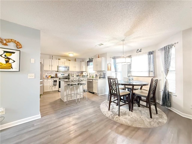 dining area with visible vents, light wood-style flooring, baseboards, and a textured ceiling