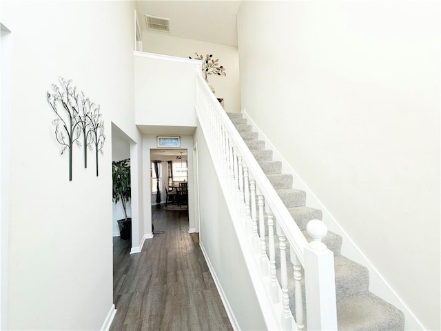 stairs with a high ceiling, wood finished floors, visible vents, and baseboards