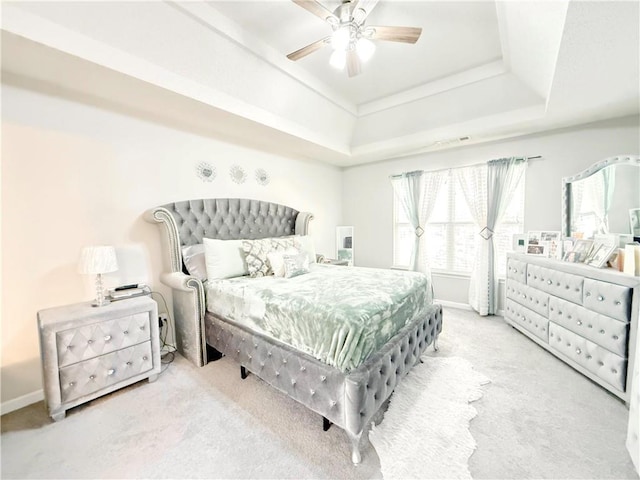 carpeted bedroom featuring a ceiling fan, a tray ceiling, multiple windows, and baseboards