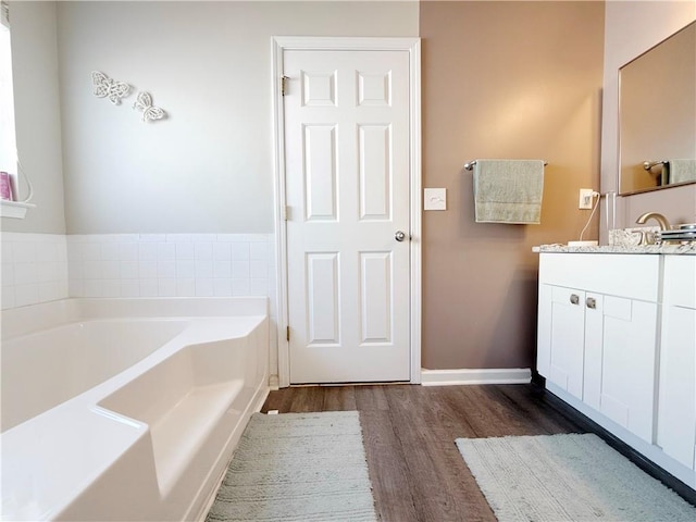 bathroom with a garden tub, vanity, baseboards, and wood finished floors