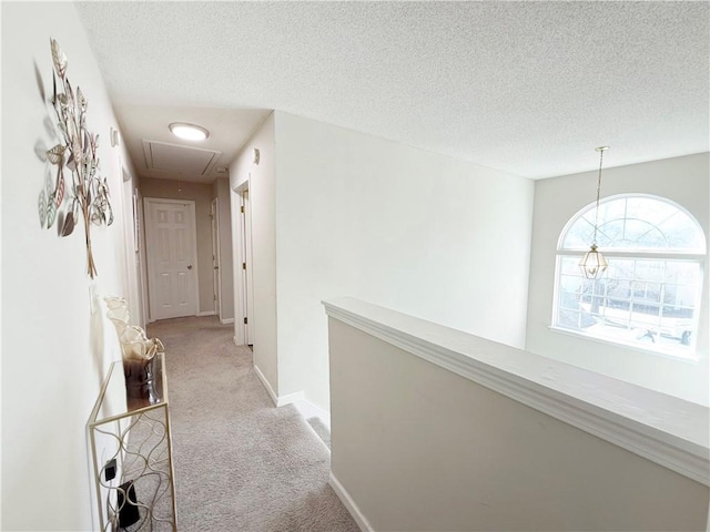 corridor featuring light carpet, attic access, baseboards, and a textured ceiling