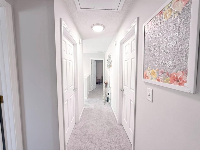 hall featuring a textured ceiling and light colored carpet