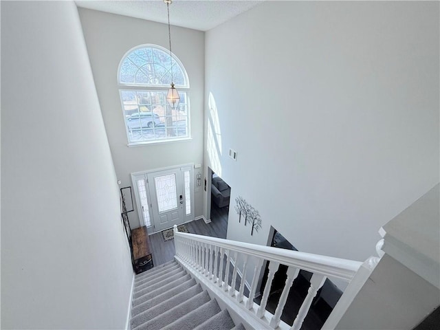 stairway with a high ceiling, a textured ceiling, and wood finished floors