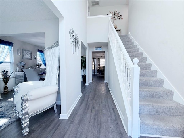 stairway with a high ceiling, visible vents, baseboards, and wood finished floors