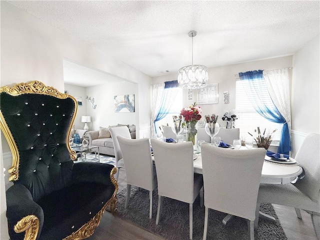 dining area featuring a healthy amount of sunlight, a textured ceiling, a notable chandelier, and wood finished floors