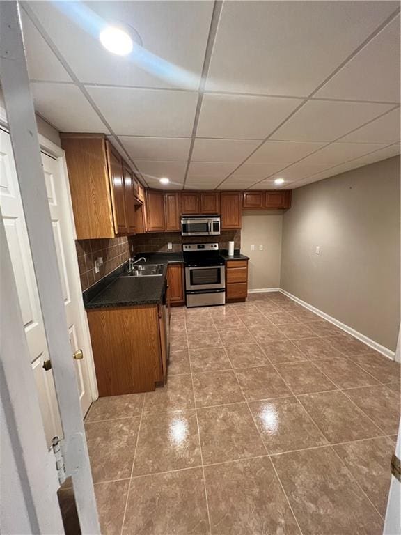 kitchen with light tile patterned floors, stainless steel appliances, sink, a drop ceiling, and decorative backsplash