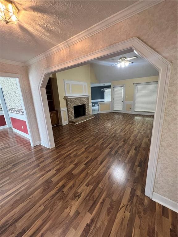 unfurnished living room featuring a fireplace, dark hardwood / wood-style flooring, ornamental molding, and ceiling fan