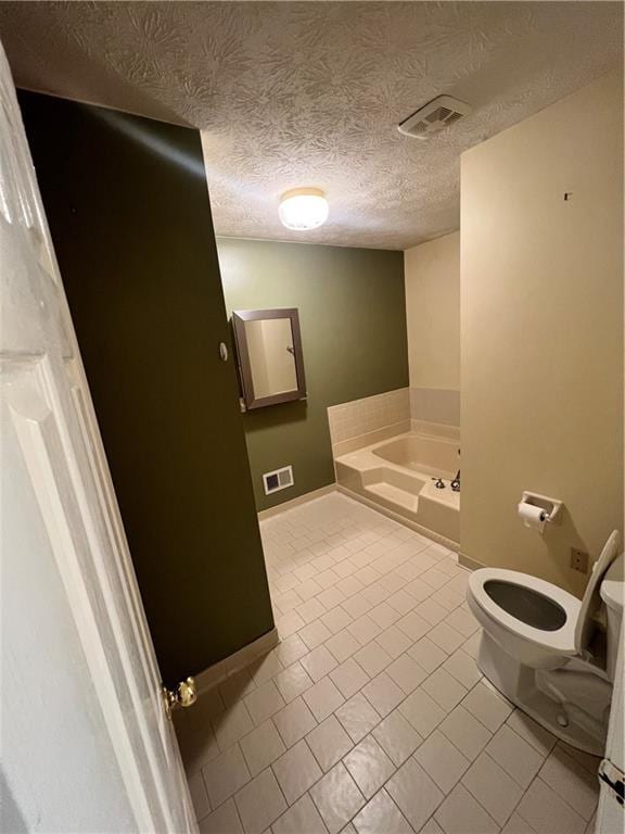 bathroom featuring a bath, tile patterned flooring, toilet, and a textured ceiling