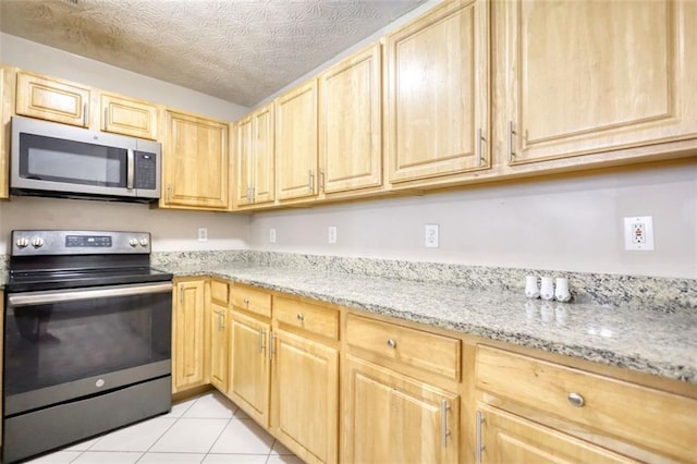kitchen featuring appliances with stainless steel finishes, light stone countertops, light tile patterned floors, and light brown cabinetry
