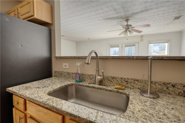 kitchen with a textured ceiling, light brown cabinets, a sink, visible vents, and fridge
