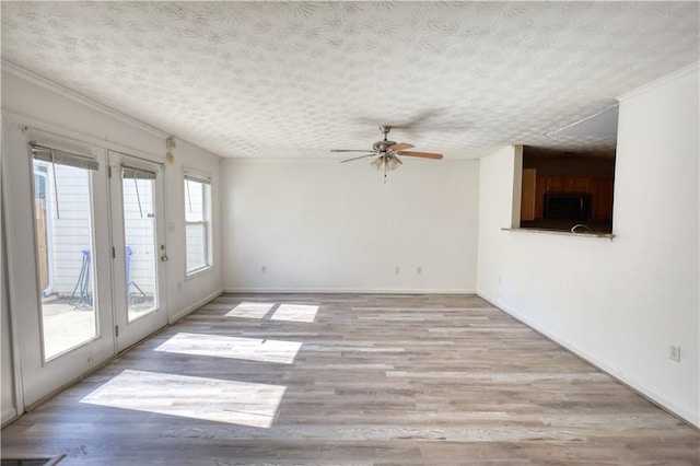 spare room with a ceiling fan, baseboards, light wood-style flooring, and a textured ceiling
