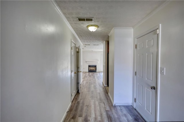 hallway with baseboards, visible vents, crown molding, a textured ceiling, and light wood-type flooring