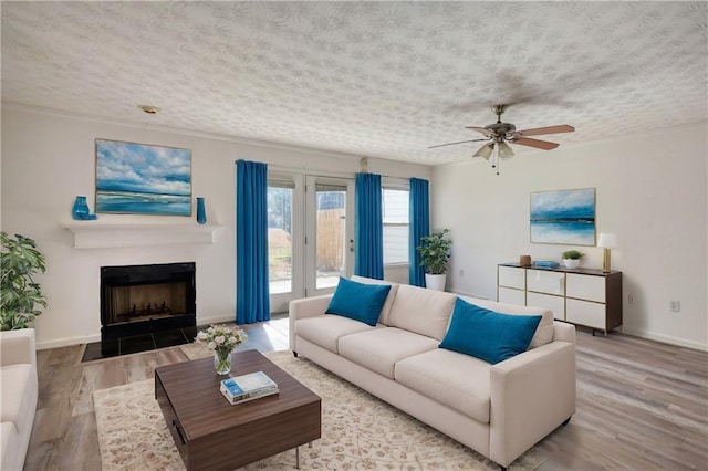 living room with light wood-style floors, a fireplace with flush hearth, baseboards, and a textured ceiling